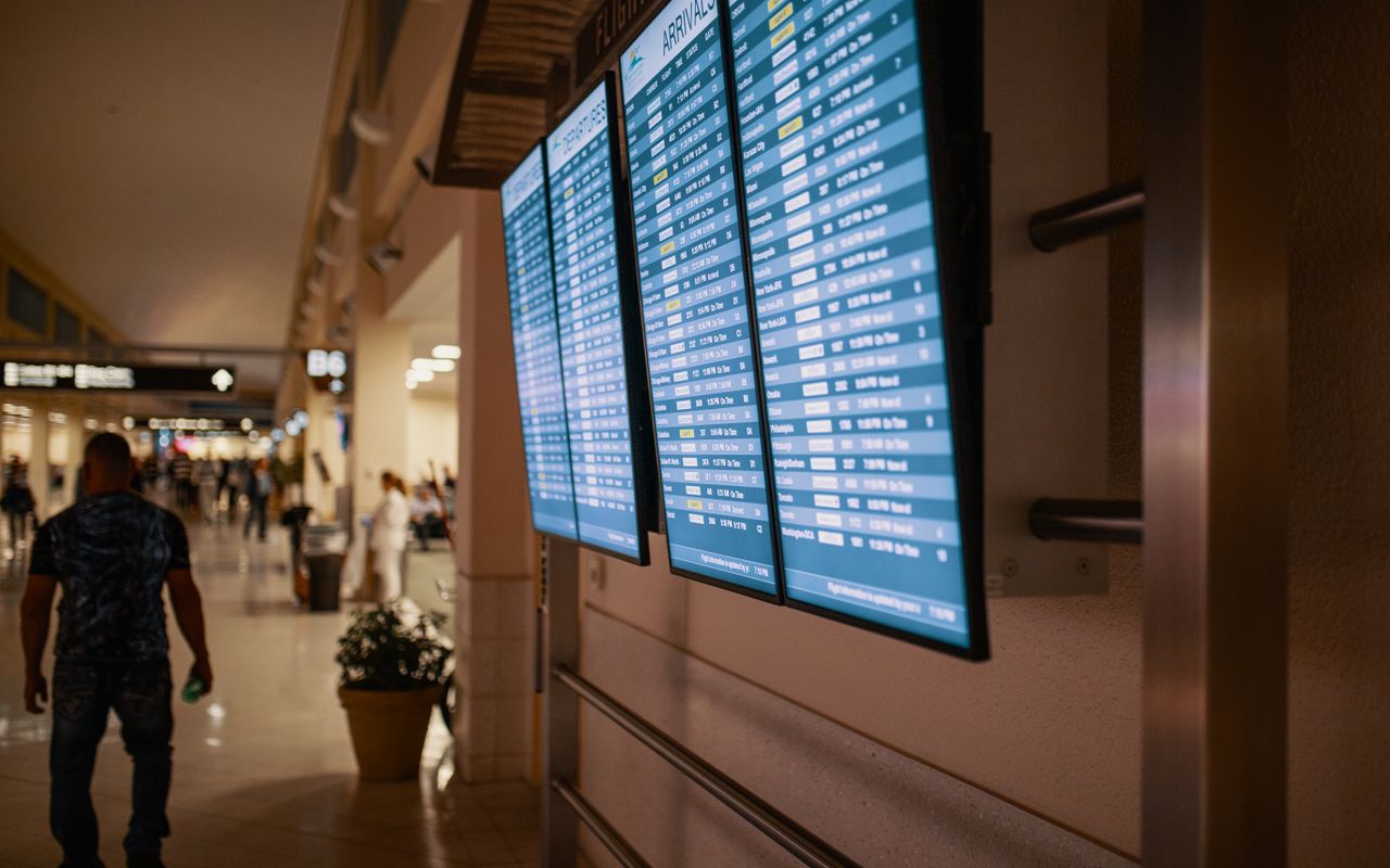 A passenger walks past the flight information wall in a terminal corridor at night