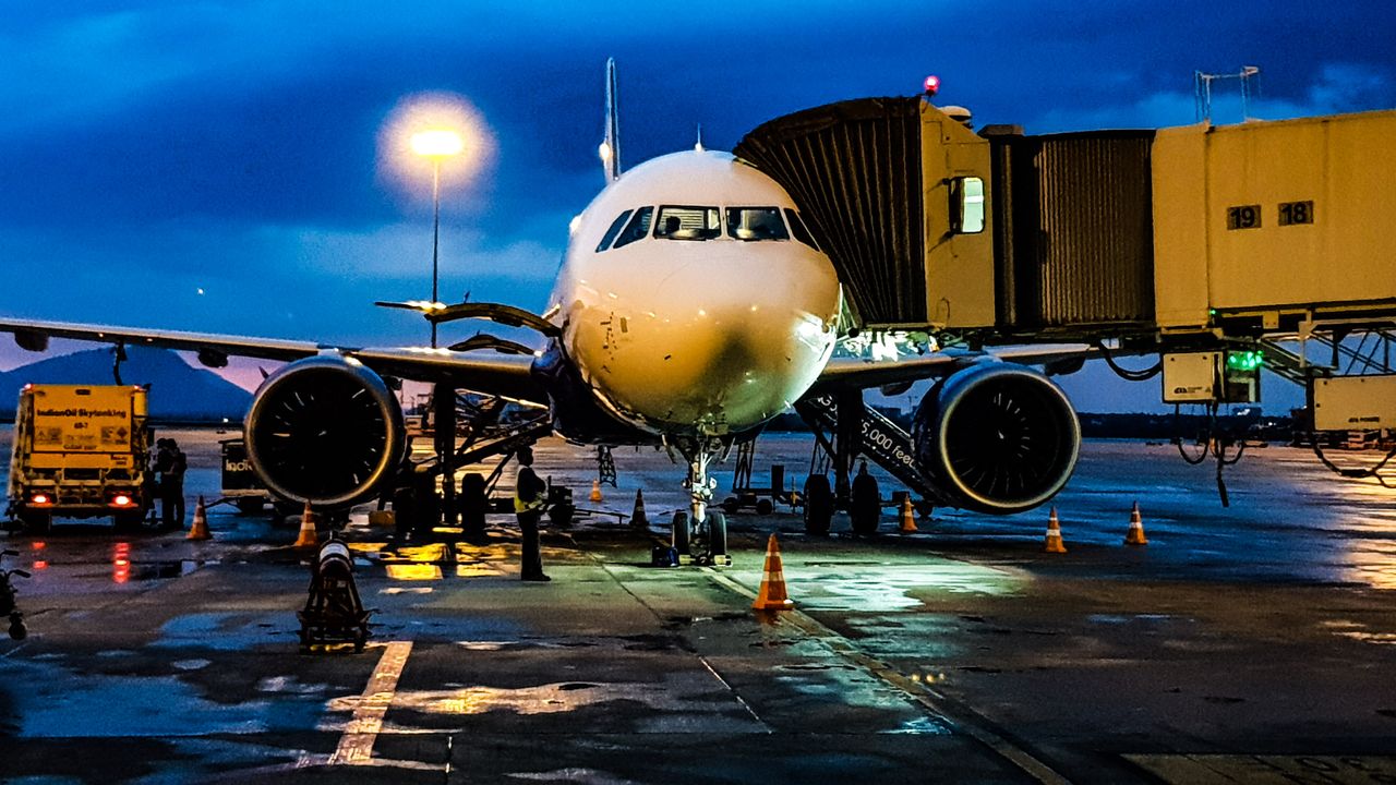 An aircraft at its stand on a wet apron at night with ground vehicles in front